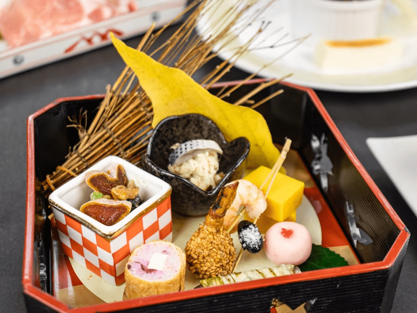 2025年11月12月《お献立の一例》旬菜: 法蓮草 干し柿胡桃和え、鰯竹紙巻、南瓜カステラ、柴漬チーズ稲荷、松葉串（海老・慈姑・黒豆）、小肌卯の花和え、香梅百合根♪