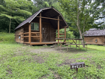 キャビンの外観です。建物前にバーベキュースペースがあります。現在はバーベキュースペース上にタープが張ってあります。向かって左側に駐車スペースがあります。