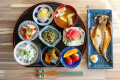 鹿嶋の貸切グランピング施設No.12 Kashima Fan Zoneの朝食は、熟成地魚の干物と旬彩小鉢５種、ご飯、味噌汁、季節フルーツが並ぶ彩り和定食。サウナでととのった身体にやさしい高タンパク&低脂質メニューで一日の活力をチャージ。地元漁港直送の鮮度、無添加仕込みの滋味深い味わいを堪能しよう。観光・ワーケーション滞在の朝に最適。今すぐ予約してヘルシーな鹿嶋モーニングを体験。ぜひどうぞ！