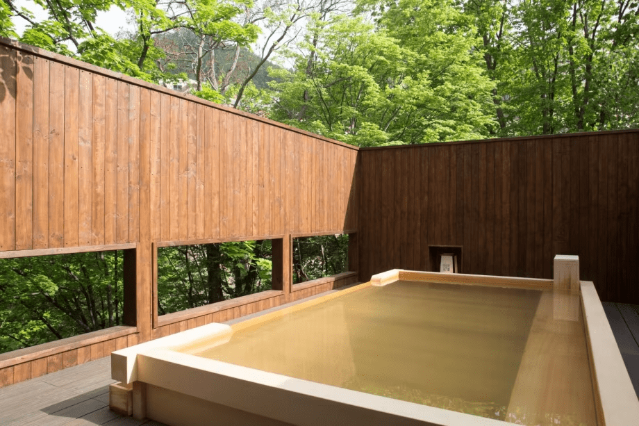 【川乃湯／檜造りの露天風呂】定山渓温泉の泉源でもある豊平川を眺めながら、ゆったりと開放的な湯浴みをお愉しみいただけます。心地よい檜の香りが深い安らぎへと誘います。