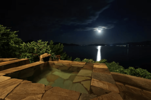 【サザエの湯／オーシャンビュー貸切展望露天風呂】かけ流しの湯に浸りながら、海と空に溶け合うような安らぎの時間を。夜には煌めく街の灯りと満天の星が広がり、幻想的な景色が心を包み込みます。