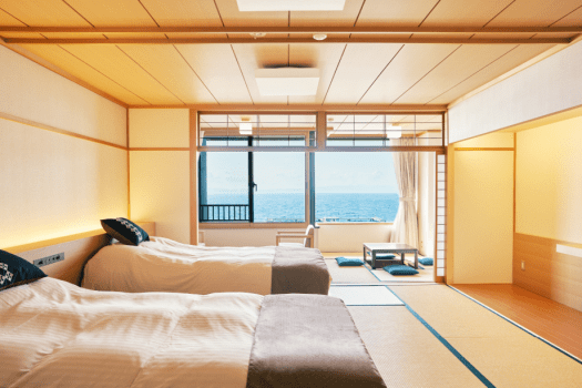 畳敷きの和室にセミダブルサイズのベッド2台とエクストラベッド1台（定員3名）をご用意しました。津軽の伝統工芸「こぎん刺し」を施したクッションもご用意しております。津軽の手仕事のあたたかさをご体感ください。窓際には掘りごたつをしつらえております。表情豊かに移ろう夕焼けをゆっくり眺めながら“旅時間”をお楽しみください。