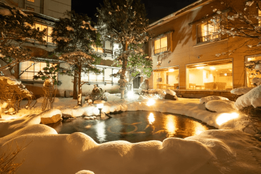 A snow-covered Japanese garden softly illuminated through the winter night.