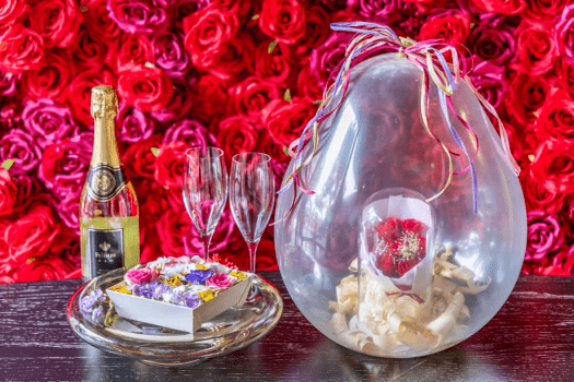 【アニバーサリープラン】華やかなローズウォールを背景に、シャンパンとグラスをご用意。さらに、バルーンの中に包まれた花束と彩り豊かなフラワーボックスが、特別な一日を優雅に演出