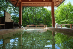 1階せせらぎの湯：木々の緑と音信川の流れを近くに感じる檜露天。四季折々の空気を吸い込みながら、アルカリの天然温泉でゆっくりおくつろぎくださいませ。