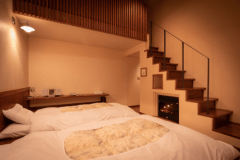 「こまくさ」寝室。正面には暖炉を模した暖房器具。実際にスイッチを入れると電気式の炎が揺らめき温風が出ます。階段を上がるとロフトがあり、昼寝などして頂くには最適の場所です。
調光付きの照明器具ですので、お好きな明るさでお過ごし頂けます（画像は最大照度）。
冬は床暖房が入ります。